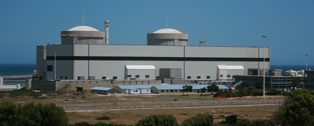 Koeberg nuclear power station. A large, grey industrial building with two rounded domes on top, situated by the sea under a clear blue sky.