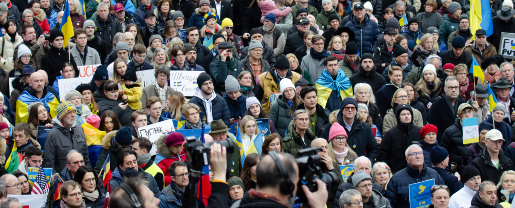 A crowd of people gather in Stockholm in support of Ukraine, some hold Ukraine flags and others hold signs