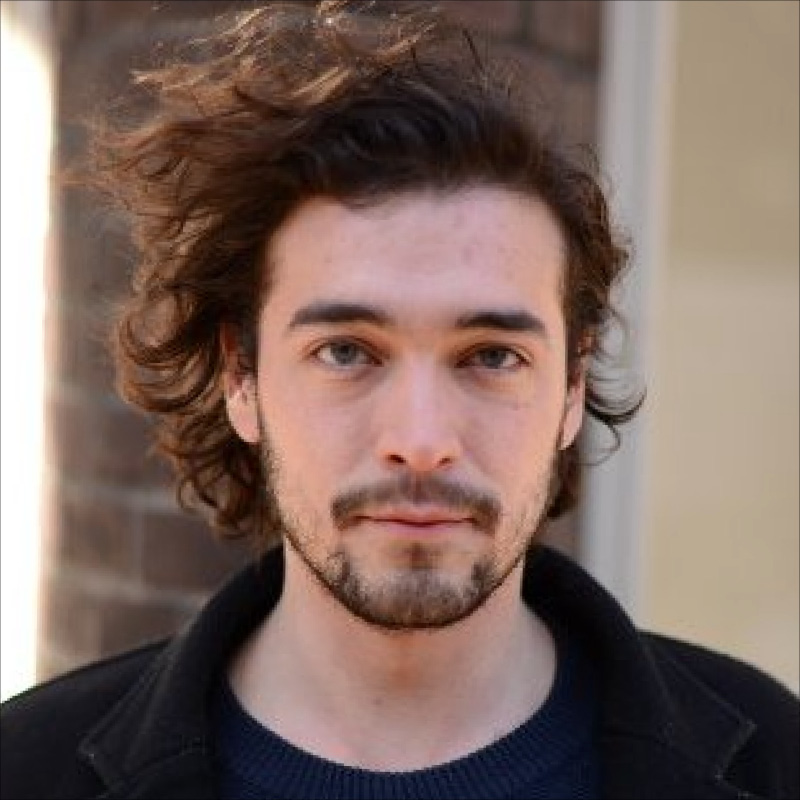 Alejandro Tauber is a young white man with windswept hair. He is wearing a black sweater and jacket